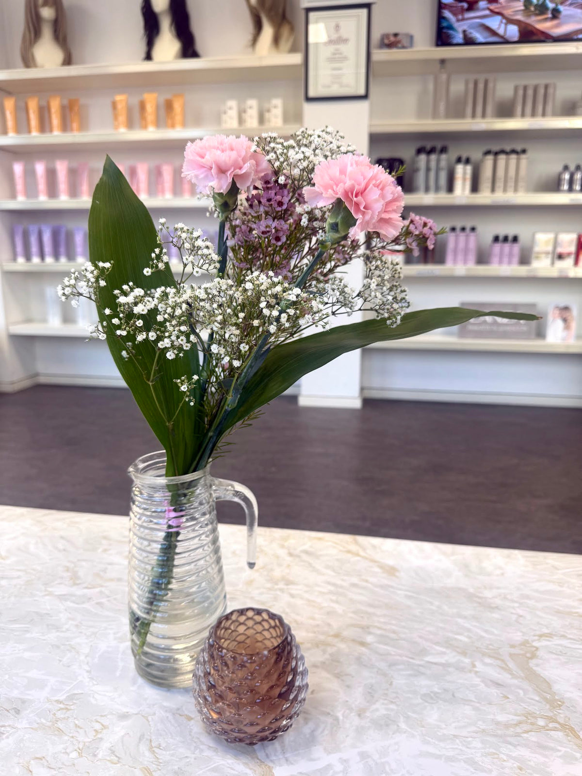 Blommor i en glaskanna på marmorbordet i Fairwithhairs salong i Uppsala, med hyllor av hårvård i bakgrunden